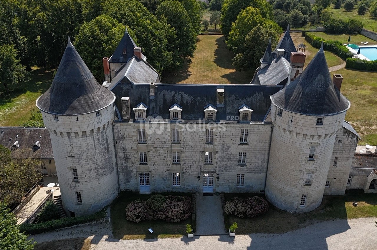 Vue aérienne d'un château en pierre avec quatre tours, entouré d'arbres et d'une pelouse.