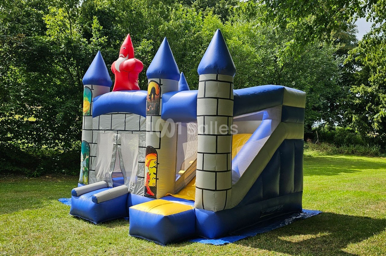 Château gonflable bleu et jaune en forme de forteresse, installé sur une pelouse entourée d'arbres.
