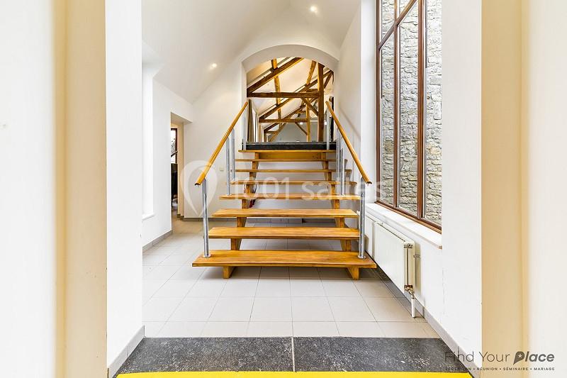 Escalier en bois avec rambardes métalliques dans un intérieur lumineux, entouré de murs blancs et d'une grande fenêtre.