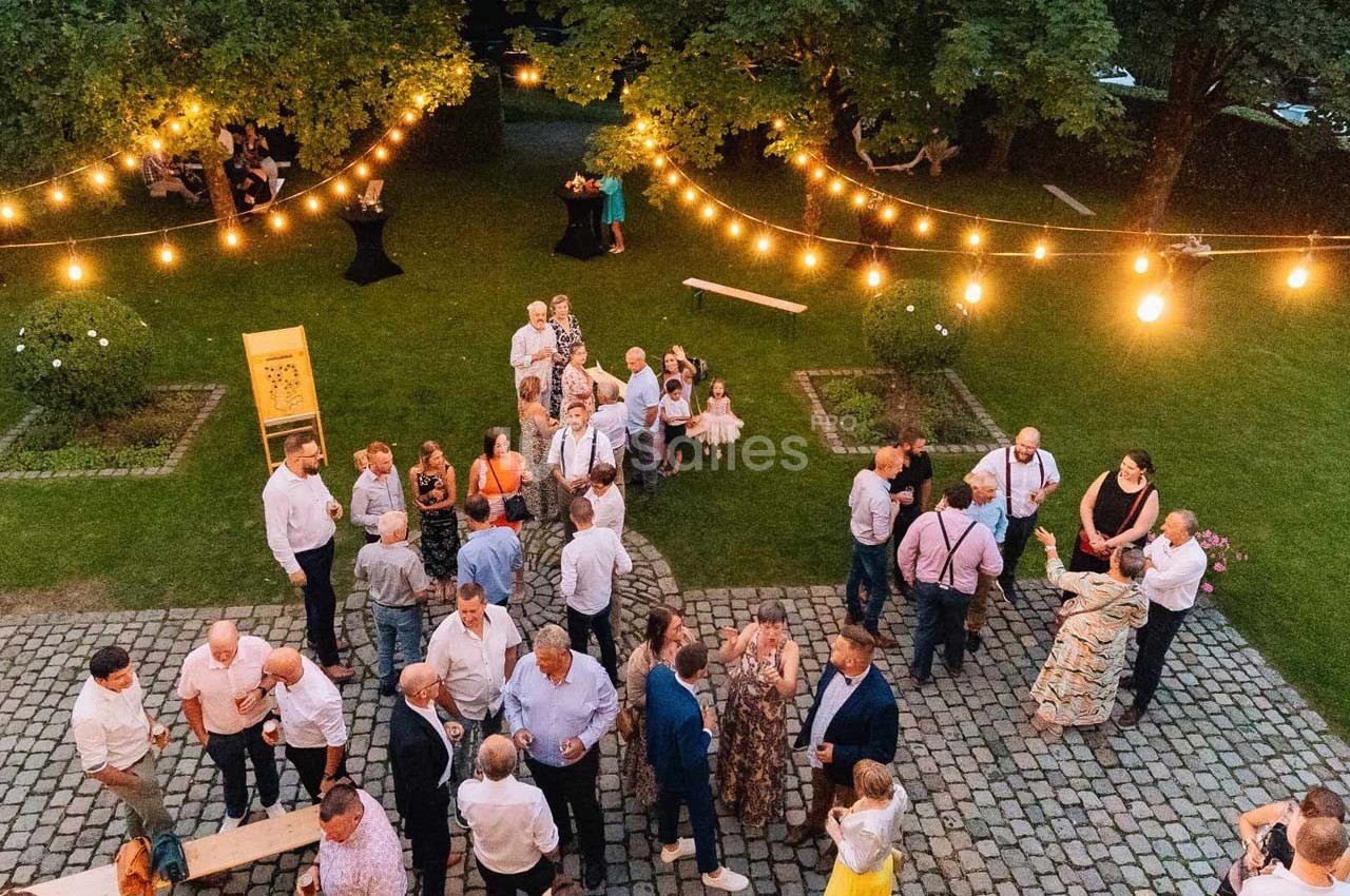 Groupe de personnes discutant dans un jardin éclairé par des guirlandes lumineuses en soirée.