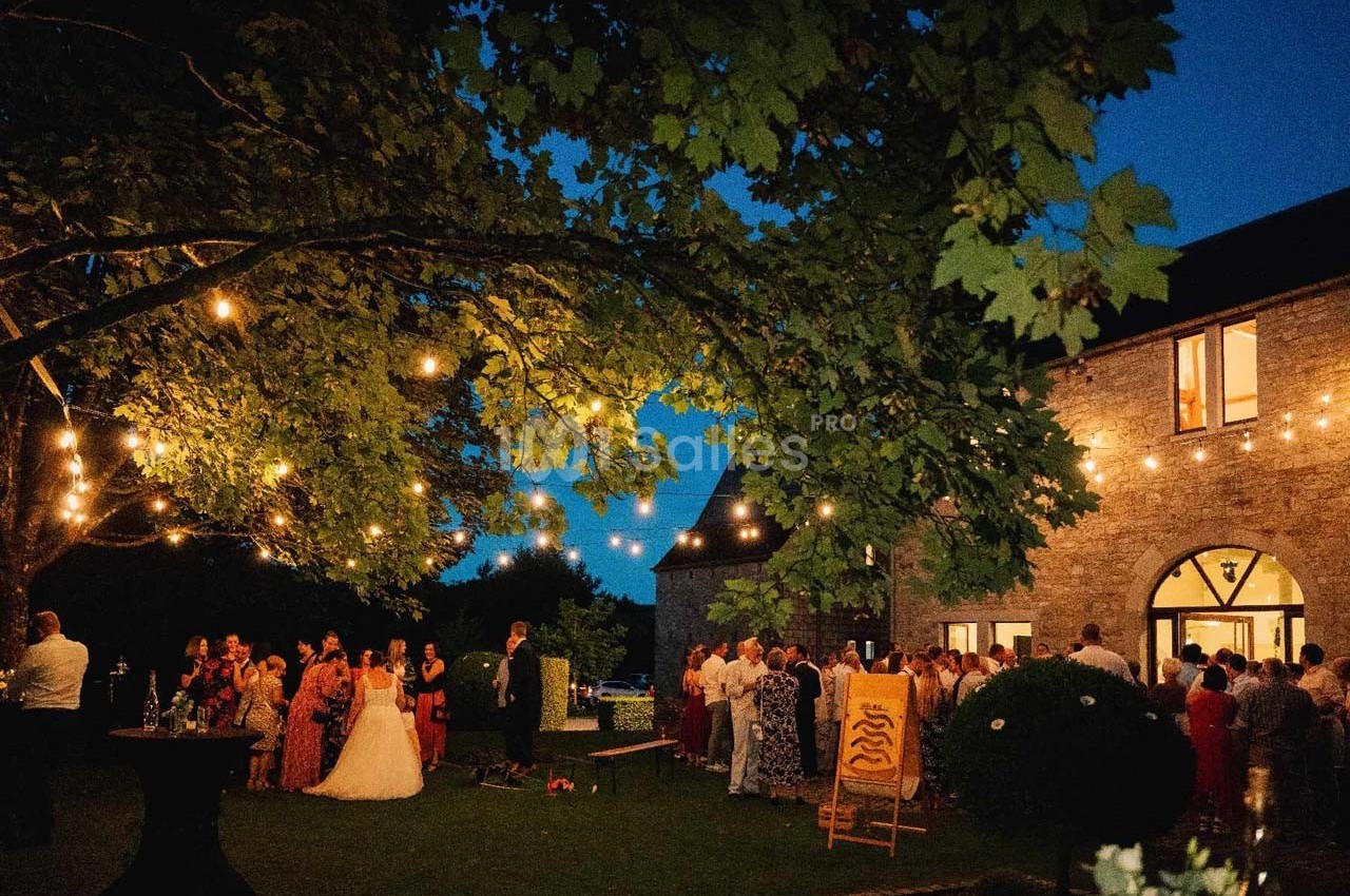 Groupe de personnes rassemblées dans un jardin éclairé par des guirlandes lumineuses, près d'un bâtiment en pierre.