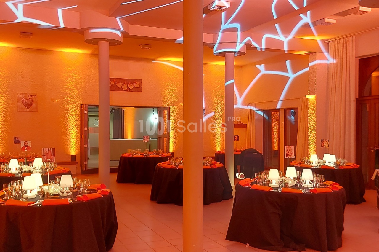 Salle de réception décorée avec des tables rondes dressées et un éclairage orange créant des motifs lumineux.