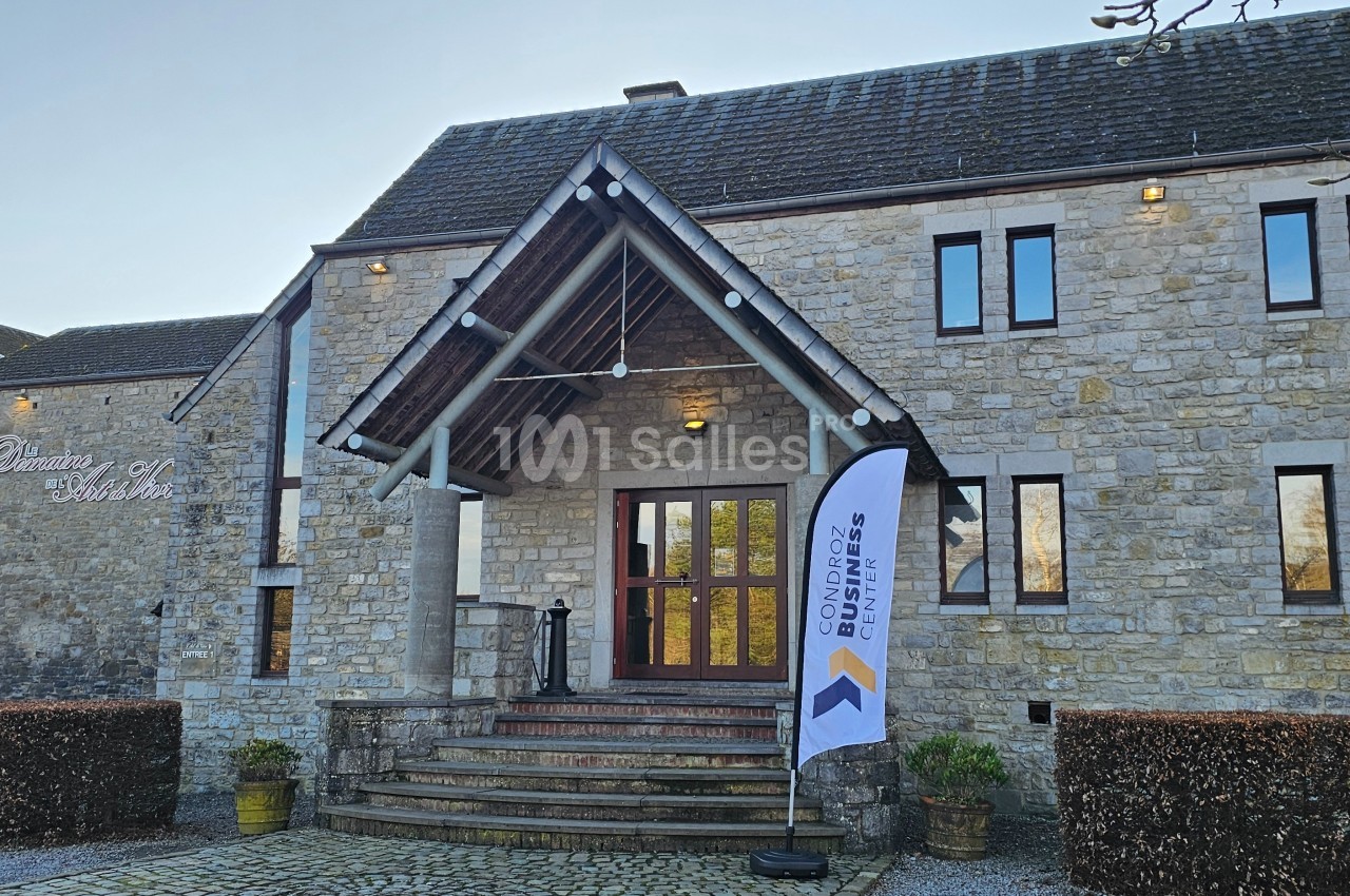 Façade d'un bâtiment en pierre avec une entrée principale, un drapeau publicitaire et une cour pavée.