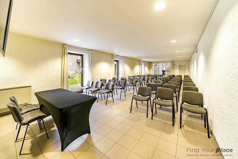 Salle de conférence lumineuse avec des rangées de chaises alignées et une table recouverte d'une nappe noire.