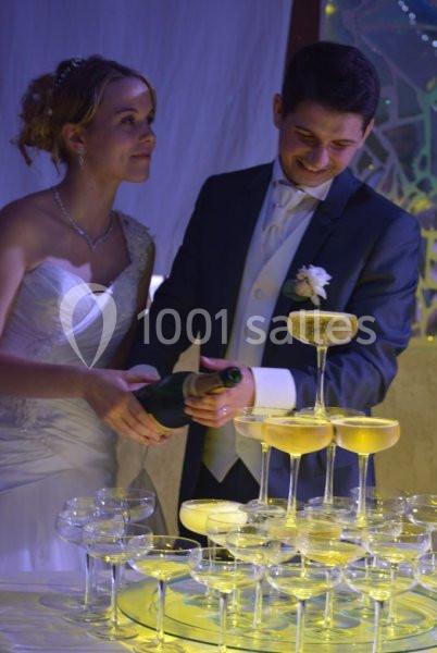 Un couple en tenue de mariage verse du champagne dans une pyramide de coupes illuminées.
