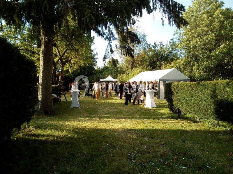 Groupe de personnes rassemblées dans un jardin avec des tentes blanches, entourées de verdure et d'arbres.