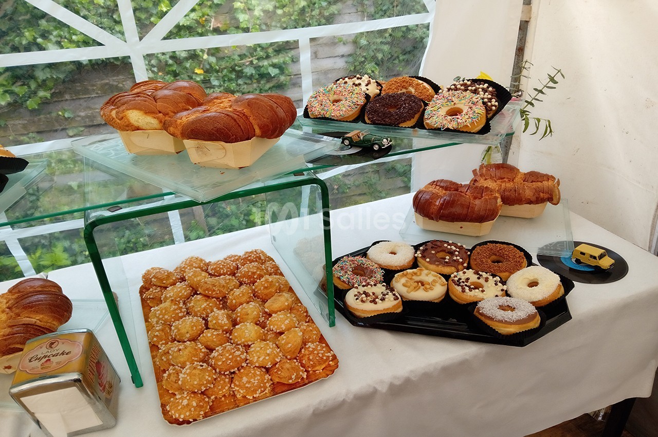 Présentation de viennoiseries, donuts et pâtisseries variées sur des plateaux dans un espace lumineux avec vue sur un jardin.