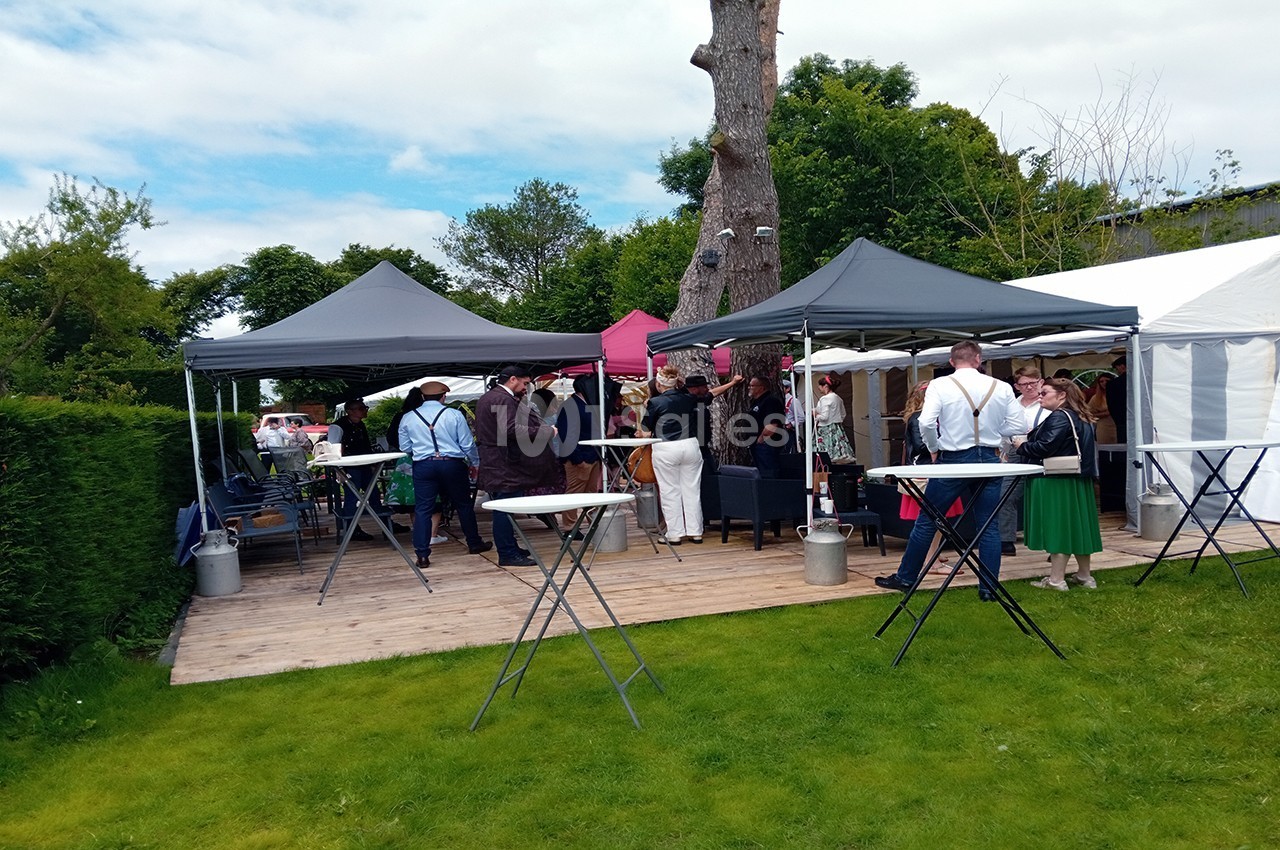 Personnes rassemblées sous des tonnelles dans un jardin, discutant autour de tables hautes lors d'un événement en plein air.