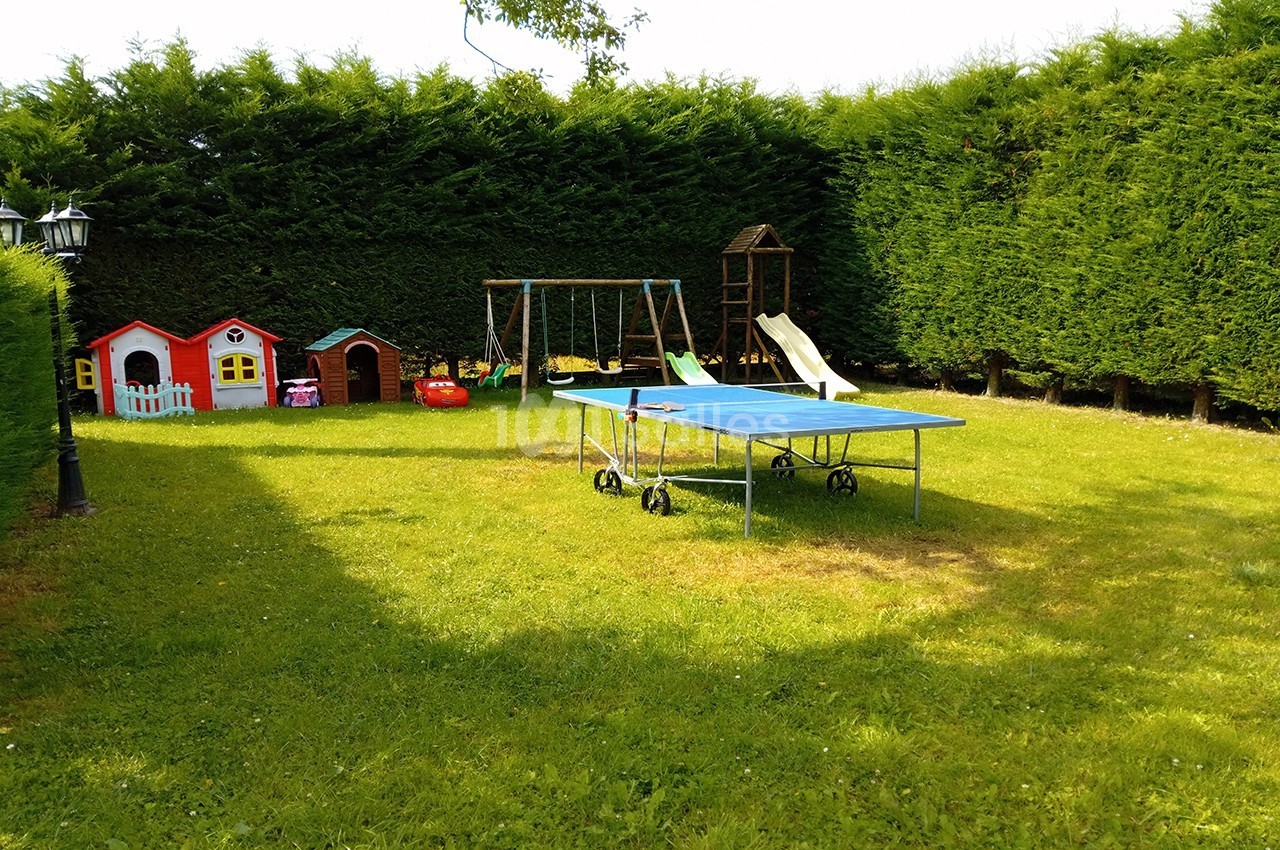 Jardin avec table de ping-pong, balançoire, toboggan et petites maisons colorées entourées de haies.