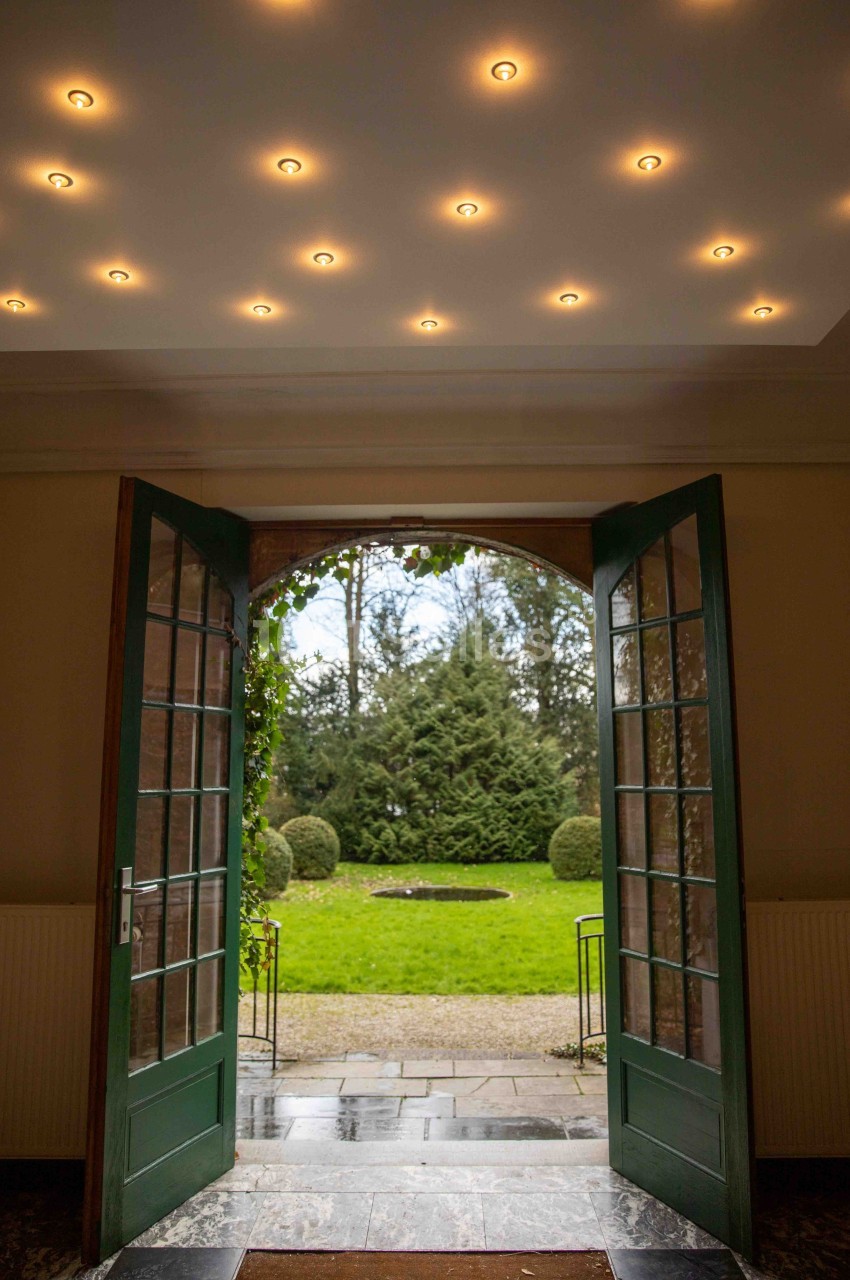 Porte-fenêtre ouverte donnant sur un jardin verdoyant avec pelouse, arbustes taillés et un bassin central.