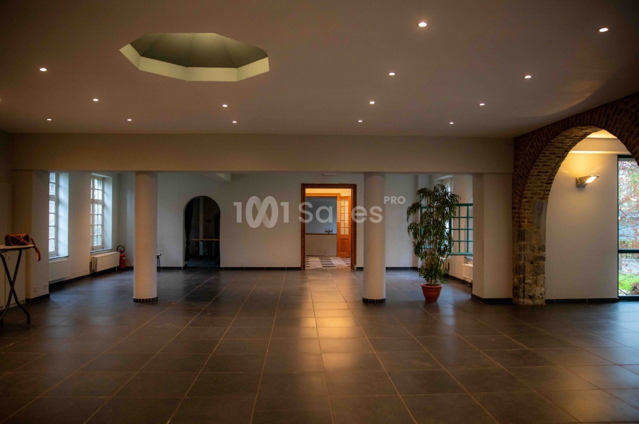 Salle spacieuse avec carrelage sombre, murs clairs, éclairage encastré et grandes fenêtres laissant entrer la lumière.