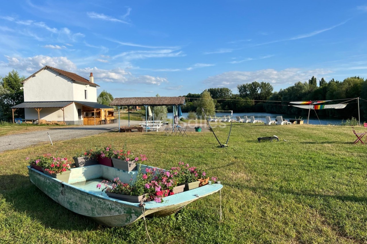 Une barque fleurie sur une pelouse, avec une maison, des tables et un plan d'eau en arrière-plan.