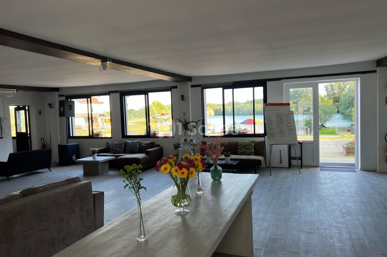 Salle lumineuse avec de grandes fenêtres, des canapés, une table ornée de fleurs et une vue sur un espace extérieur…