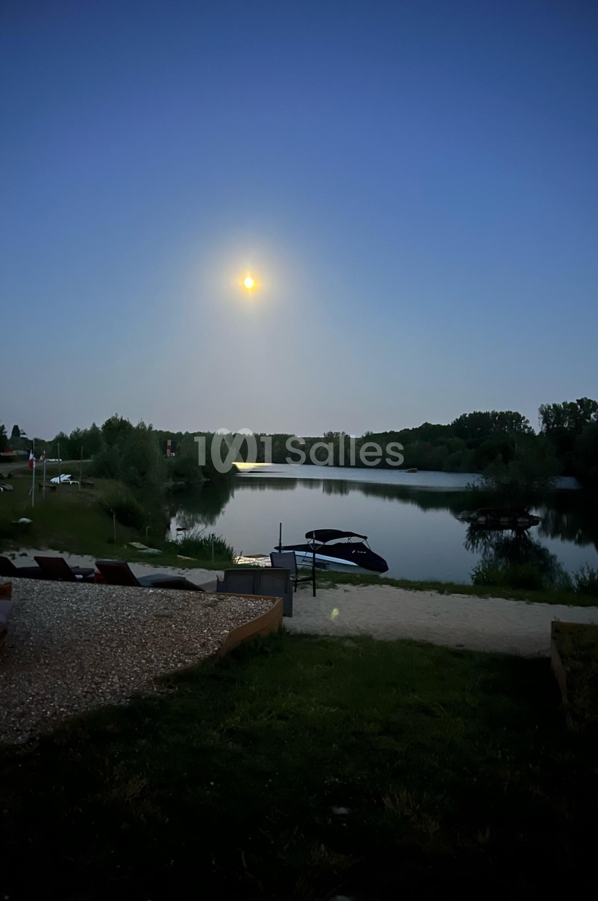 Vue nocturne d'un lac calme éclairé par la lune, entouré de végétation et de quelques bateaux amarrés.