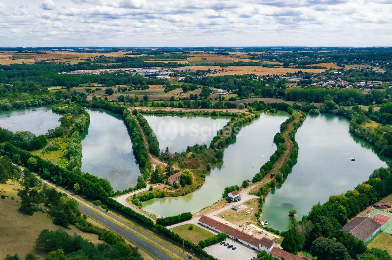 Vue aérienne de trois étangs entourés de végétation, avec des champs et des infrastructures en arrière-plan.