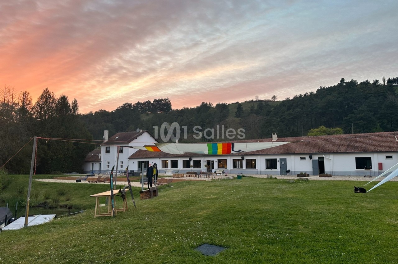 Bâtiment blanc avec toit en tuiles, décoré d'une bannière colorée, entouré de verdure au coucher du soleil.