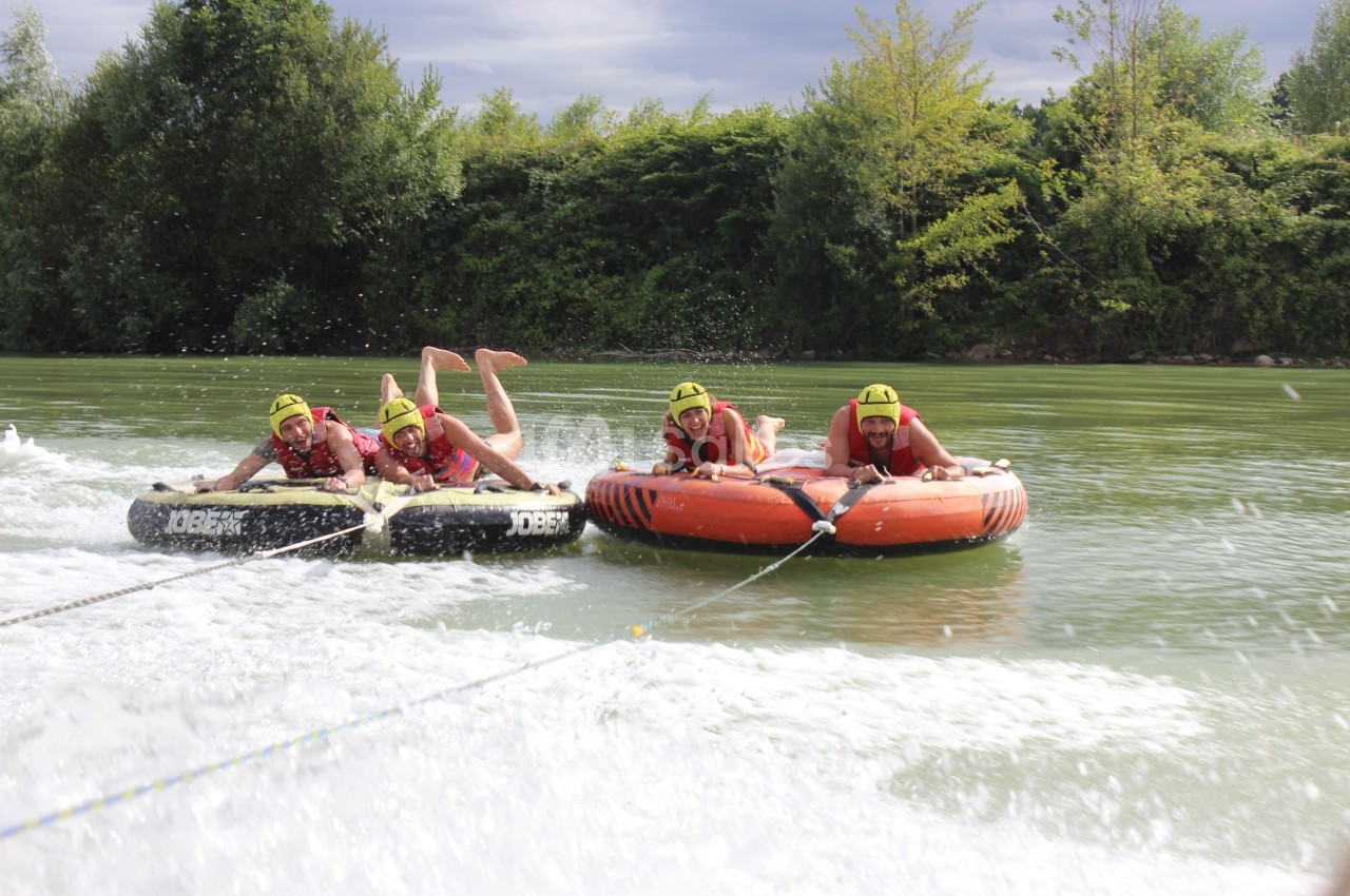 Des personnes portant des gilets de sauvetage s'accrochent à des bouées tractées sur une rivière entourée de végétation.