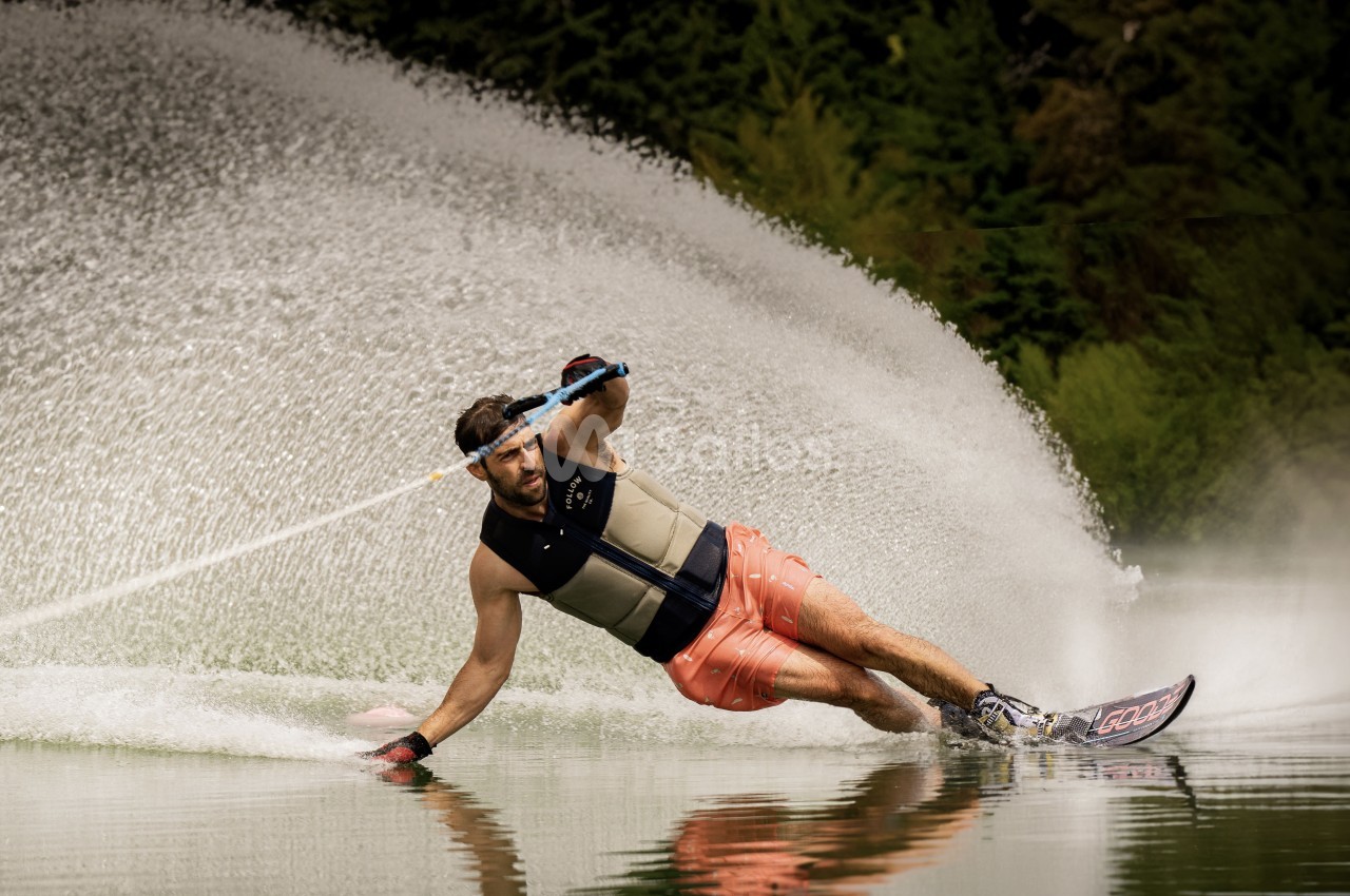 Un homme fait du ski nautique sur un lac, créant une éclaboussure d'eau en effectuant un virage serré.