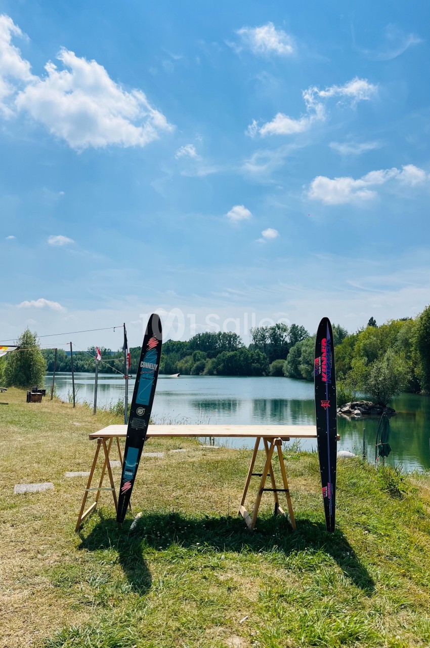Deux skis nautiques posés contre une table en bois, près d'un lac entouré de verdure sous un ciel dégagé.