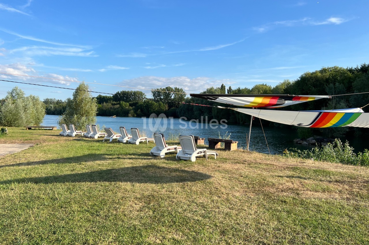 Chaises longues alignées sur une pelouse au bord d'une rivière, avec un grand auvent coloré tendu au-dessus.