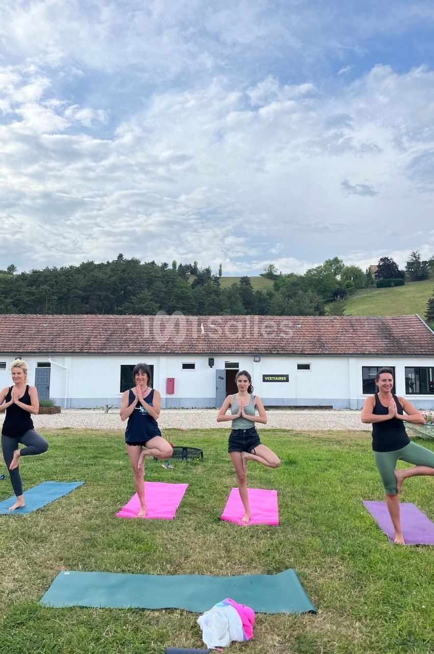 Quatre femmes pratiquant le yoga en posture de l'arbre sur des tapis colorés dans un espace extérieur herbeux.