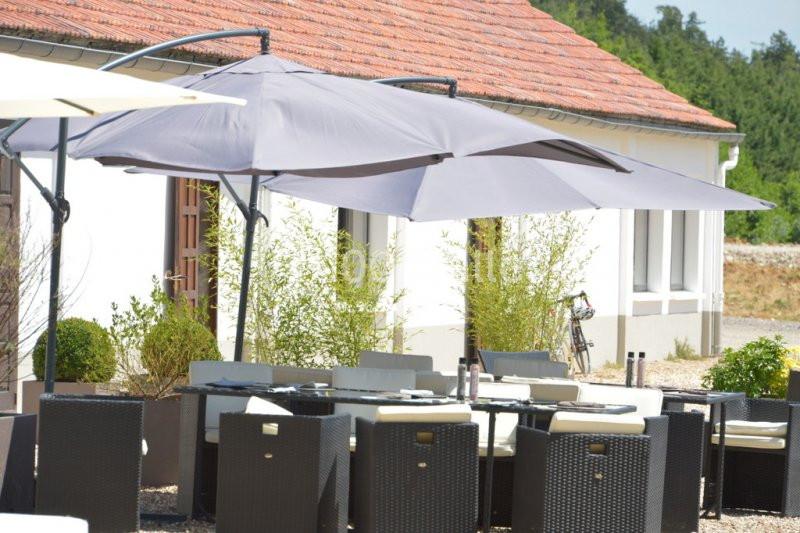 Terrasse aménagée avec des tables et chaises en rotin sous de grands parasols gris, près d'un bâtiment blanc.