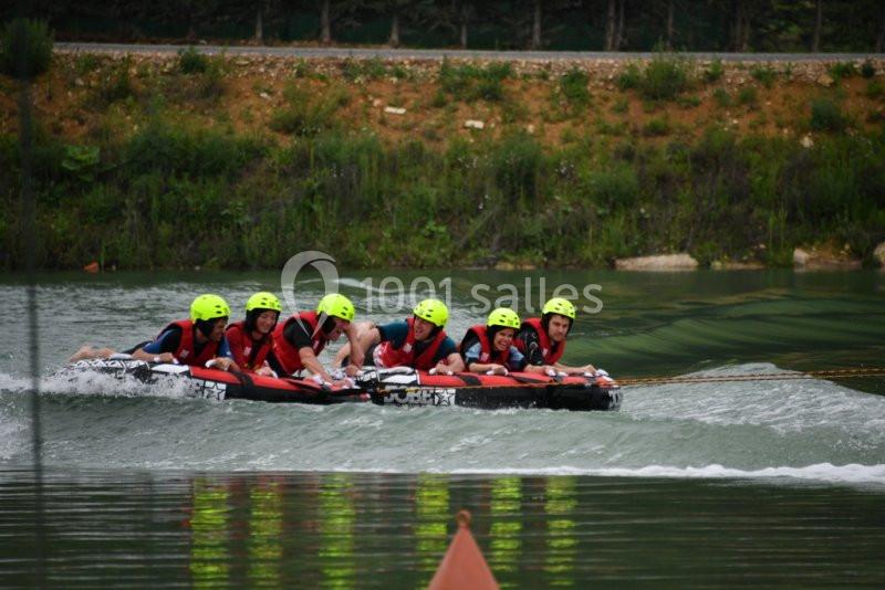 Des personnes portant des casques et des gilets de sauvetage glissent sur l'eau sur une grande bouée tractée.