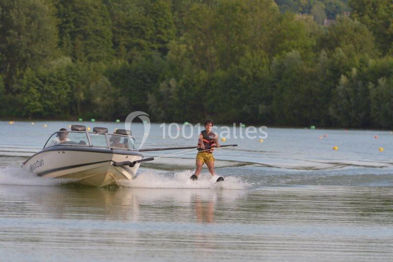 Une personne fait du ski nautique tirée par un bateau sur un lac entouré de végétation.