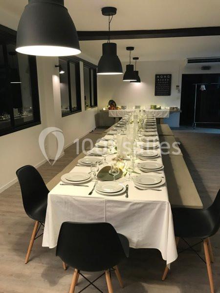 Table dressée avec nappes blanches, vaisselle et verres alignés dans une salle moderne éclairée par des suspensions noires.