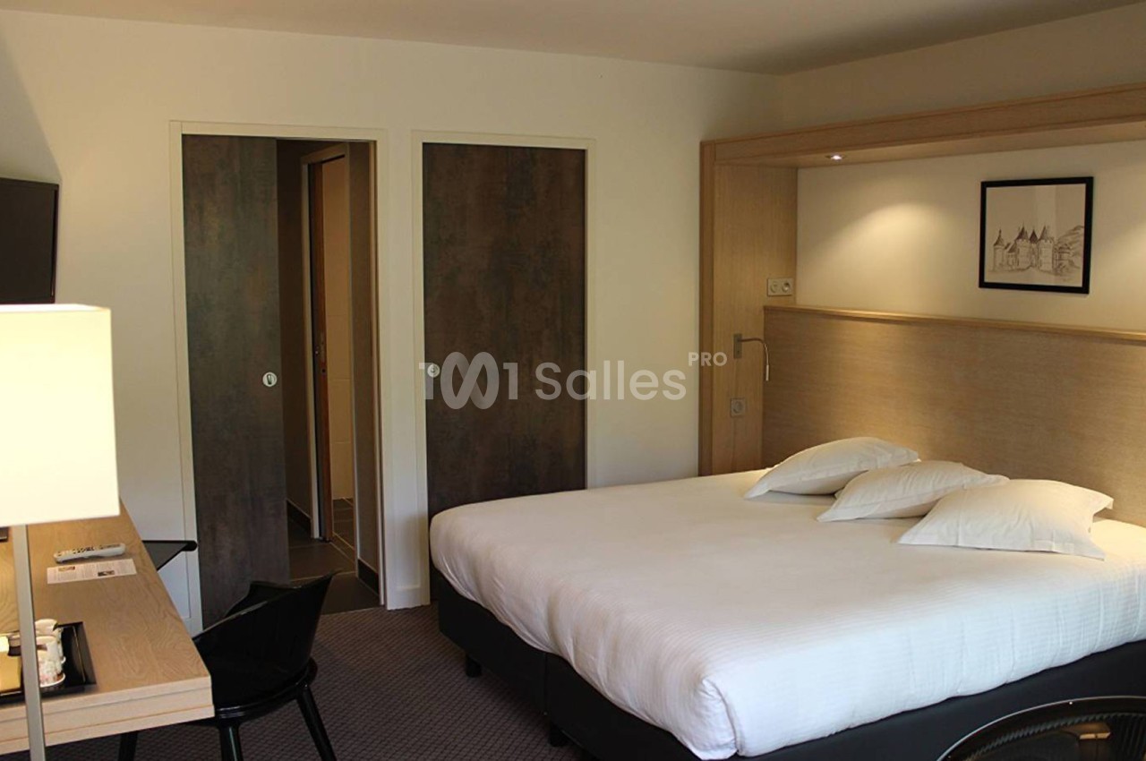 Chambre d'hôtel avec lit double, bureau équipé, télévision murale et portes menant à une salle de bain.