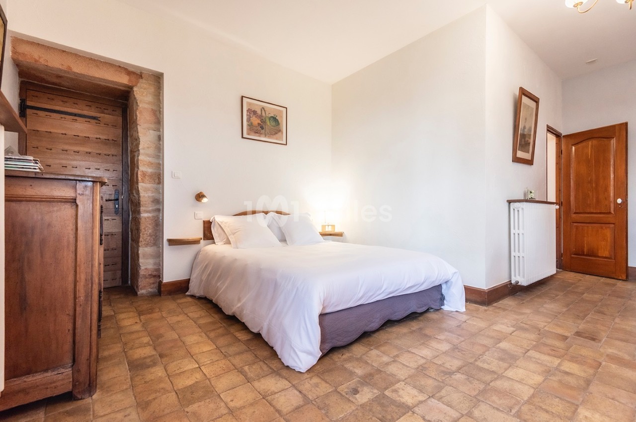 Chambre lumineuse avec lit double, sol en carreaux de terre cuite, mobilier en bois et porte en bois massif.