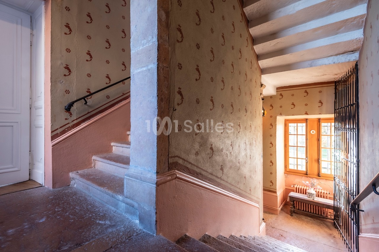 Escalier intérieur ancien avec murs ornés de motifs, rampe en métal et lumière naturelle entrant par une fenêtre.