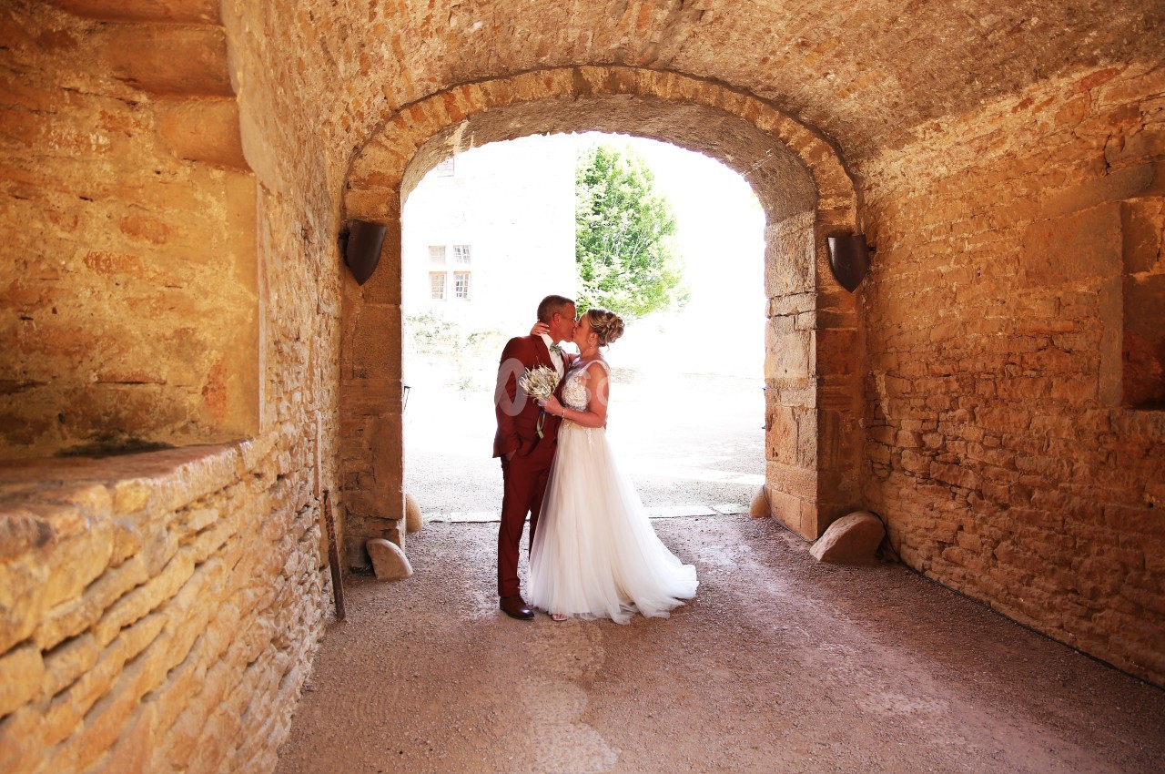 Un couple de mariés s'embrasse sous une arche en pierre, baignée de lumière naturelle.