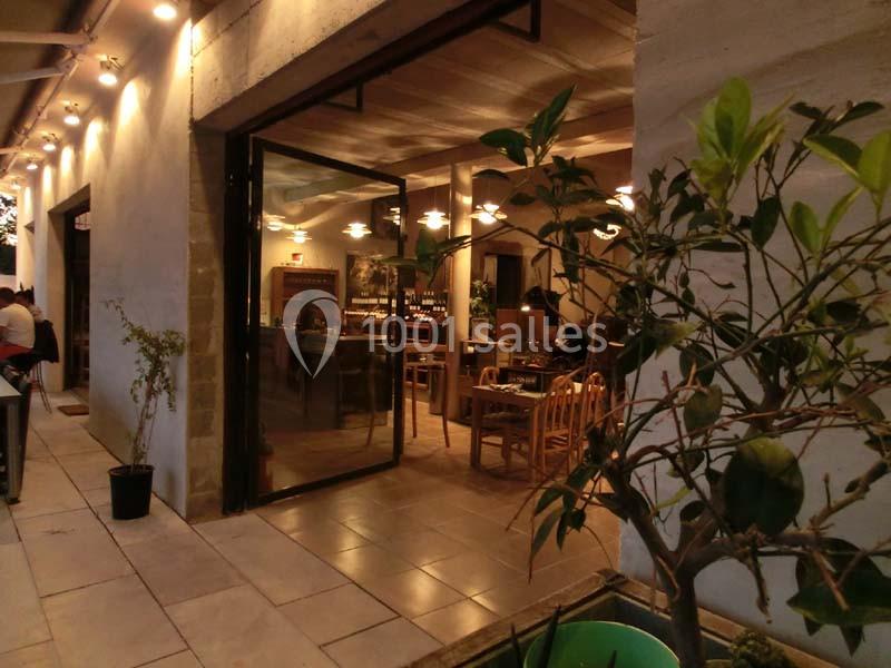 Vue extérieure d'un restaurant avec une entrée vitrée ouverte, éclairage chaleureux et plantes en premier plan.