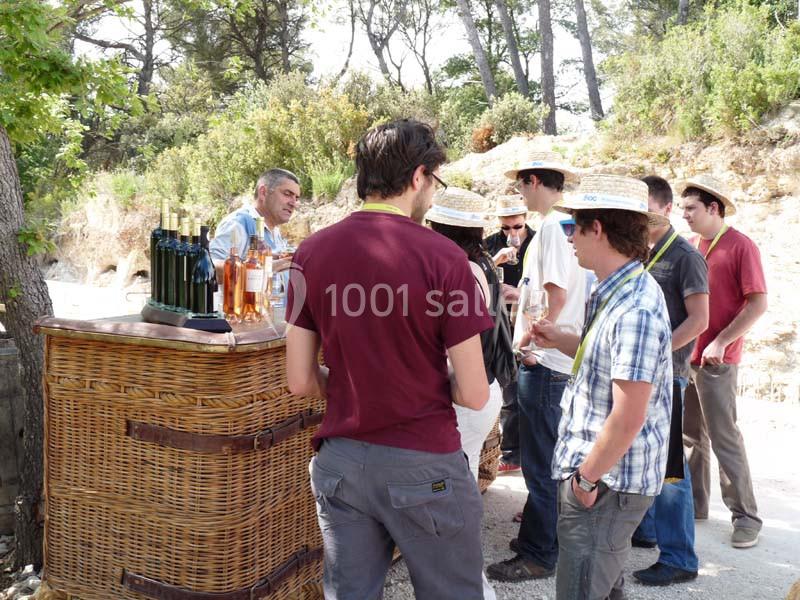 Groupe de personnes dégustant du vin autour d'un stand en plein air, entouré de végétation.