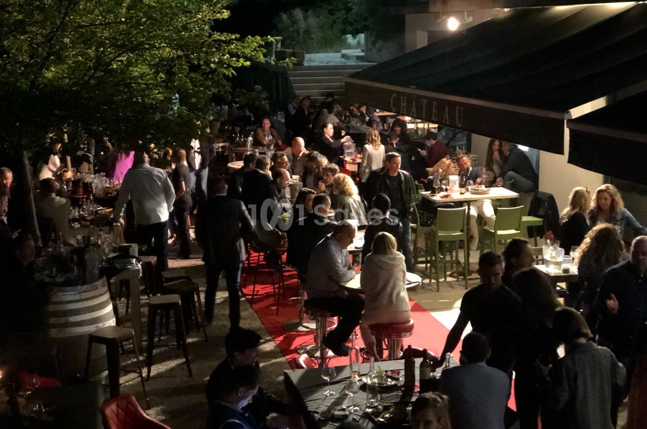 Terrasse animée en soirée avec des tables occupées par des convives, éclairage tamisé et ambiance conviviale.