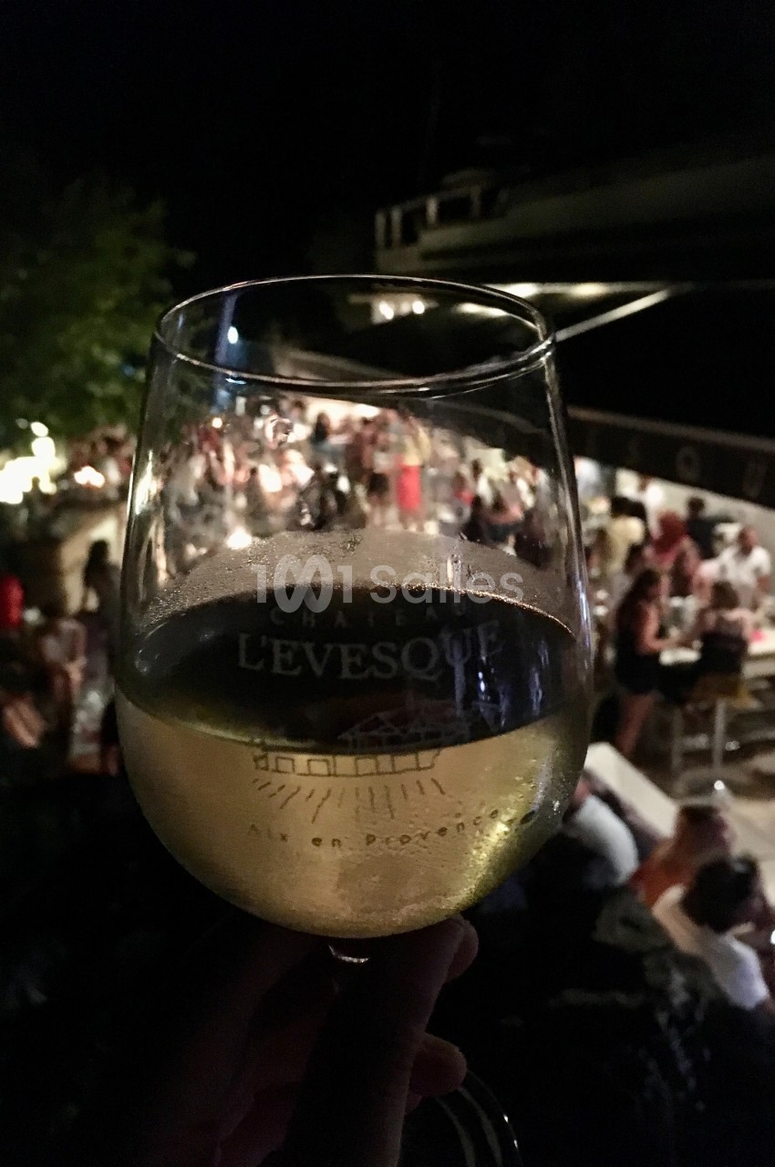 Verre de vin blanc tenu devant une scène animée en soirée, avec des personnes attablées en arrière-plan.