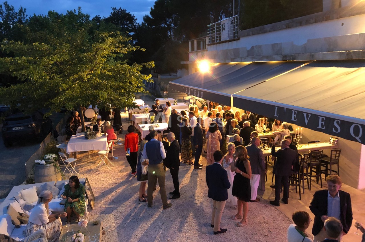 Groupe de personnes réunies en soirée en extérieur, près de tables et d'un bâtiment éclairé.