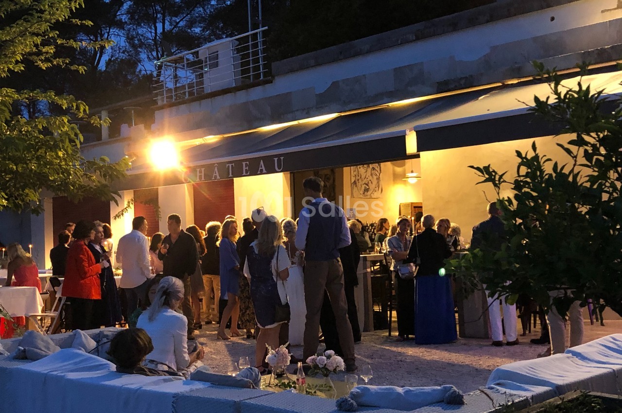 Groupe de personnes rassemblées en soirée devant un bâtiment éclairé, ambiance conviviale en extérieur.