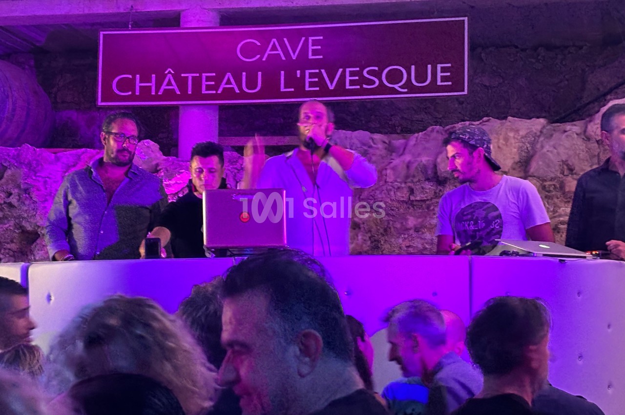 Un groupe de DJ anime une soirée dans une cave éclairée en violet, avec un public en arrière-plan.