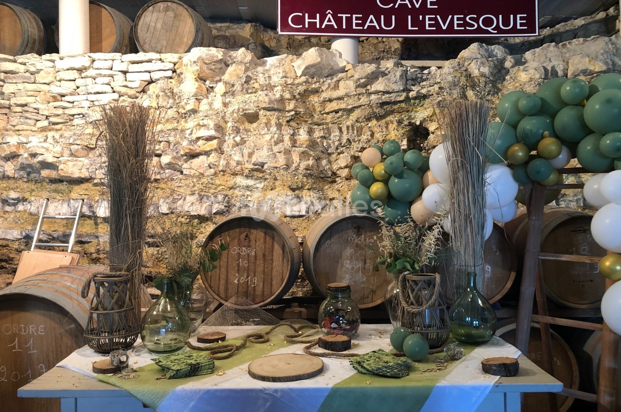 Table décorée avec des éléments naturels devant des tonneaux en bois dans une cave voûtée en pierre.