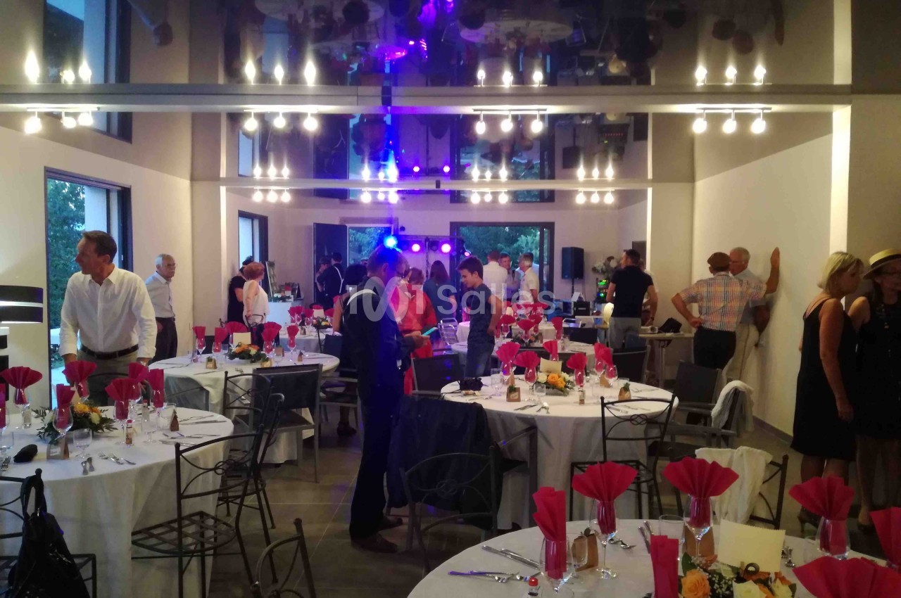Salle de réception décorée avec des tables dressées, des invités debout discutant et des lumières colorées en arrière-plan.