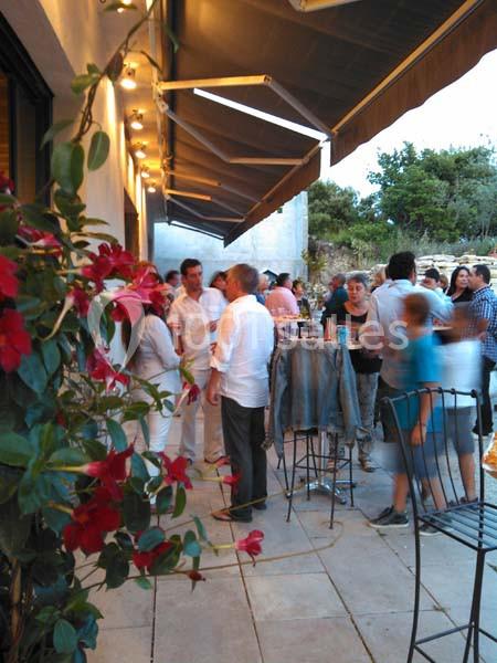 Groupe de personnes discutant sur une terrasse extérieure, entourée de fleurs et de mobilier de jardin.