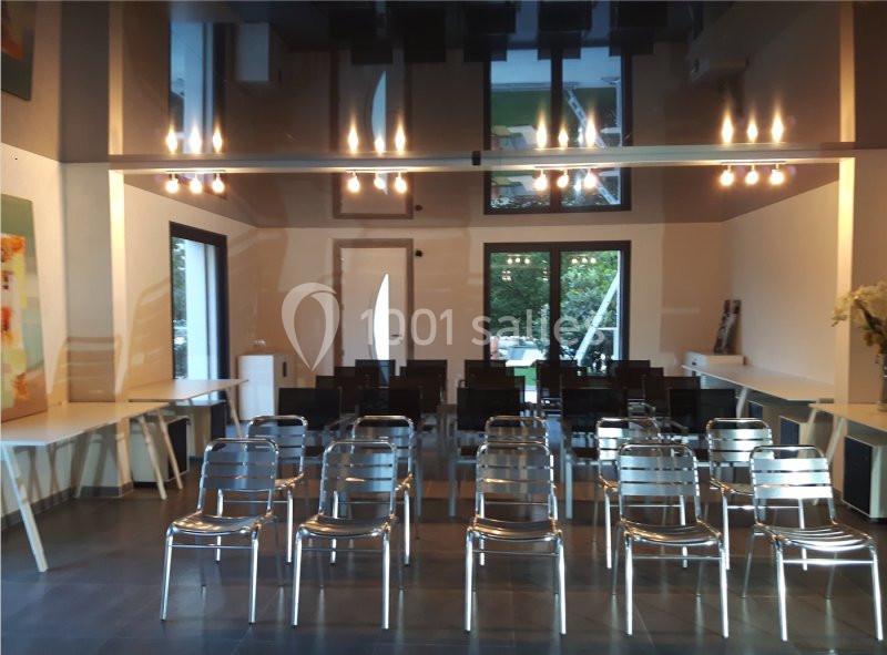 Salle moderne avec des chaises métalliques alignées face à une porte vitrée, éclairée par des suspensions lumineuses.
