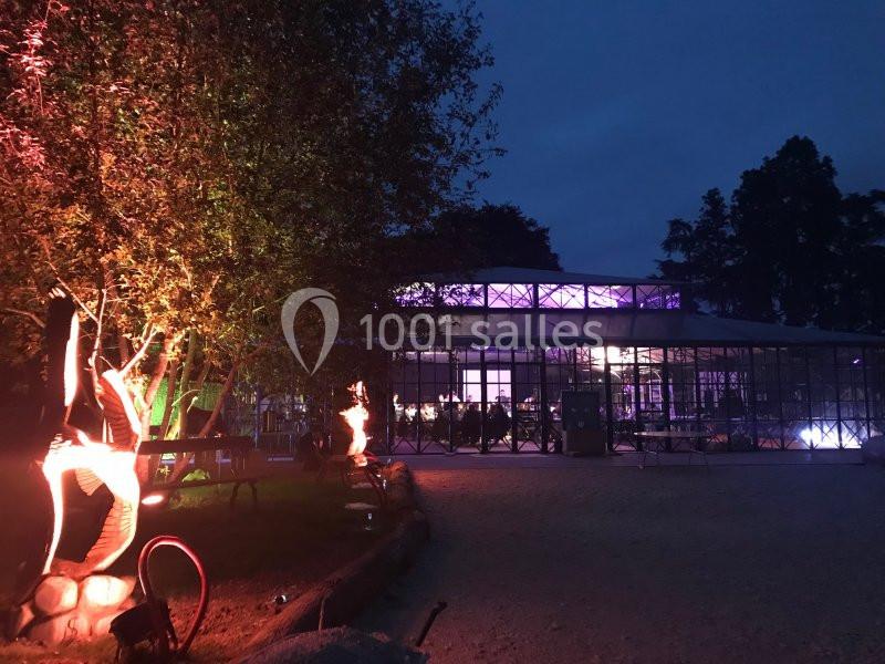 Vue nocturne d'un bâtiment vitré éclairé par des lumières violettes, entouré d'arbres et d'installations lumineuses.