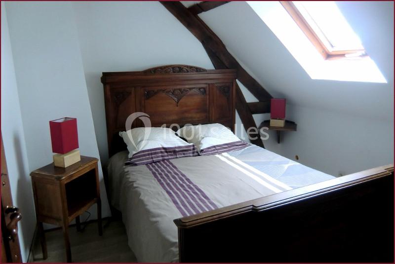 Chambre avec lit double en bois, table de chevet, lampes rouges et lumière naturelle provenant d'une fenêtre de toit.