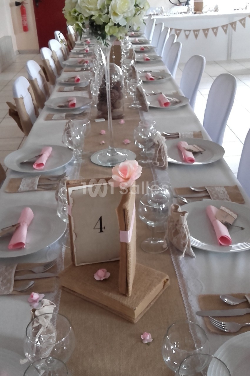 Table de réception décorée avec des nappes en toile de jute, des fleurs, des serviettes roses et un centre de table floral.