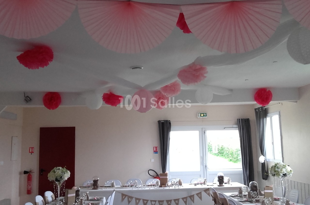 Décoration de salle avec des lanternes et pompons roses et blancs suspendus, table dressée en arrière-plan.