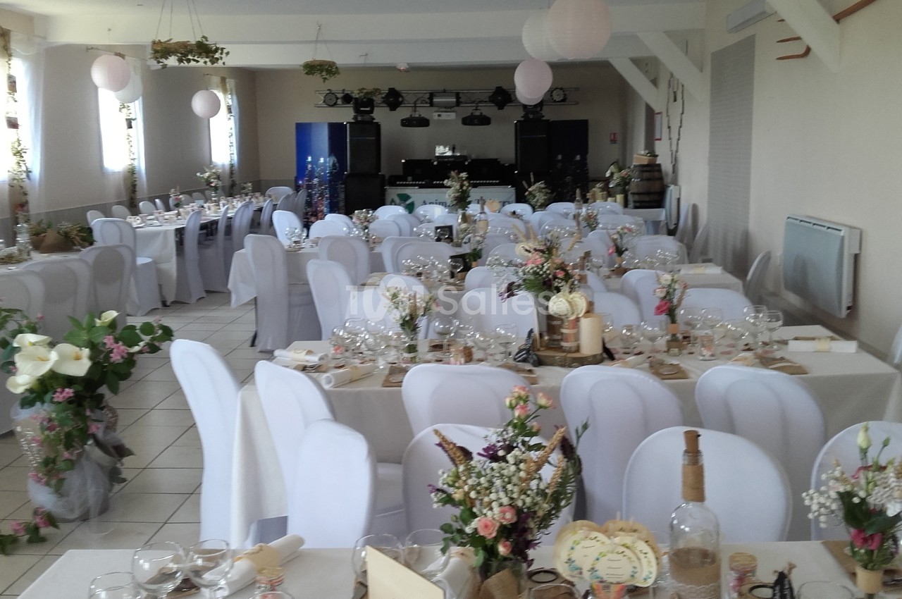 Salle de réception décorée pour un événement, avec des tables dressées, nappes blanches et arrangements floraux.