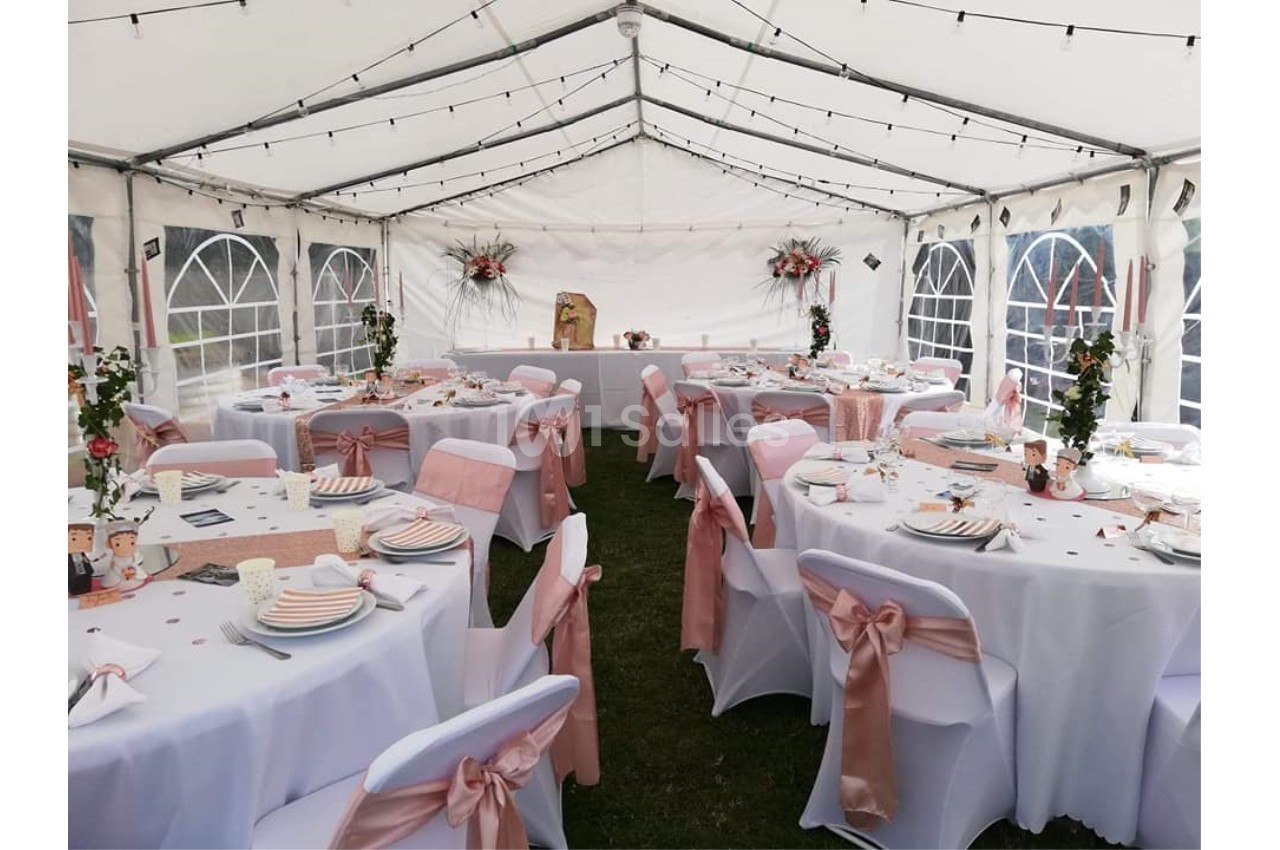 Salle de réception sous chapiteau blanc, décorée de nappes blanches et rubans roses, avec tables dressées pour un événement.